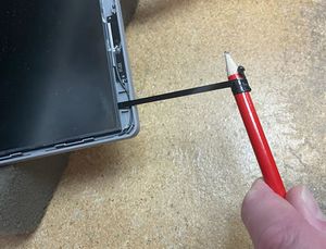 Image of pencil being used to gently remove laptop screen adhesive.